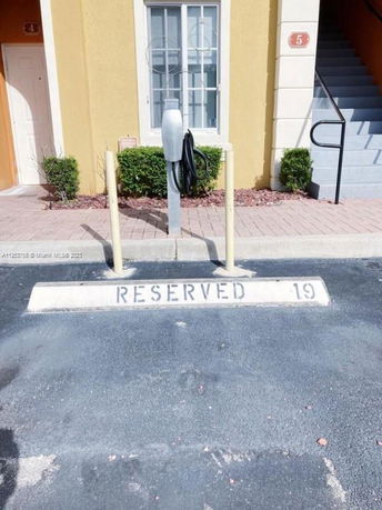 Outdoor parking space marked as reserved with a charging station in front of a building entrance.