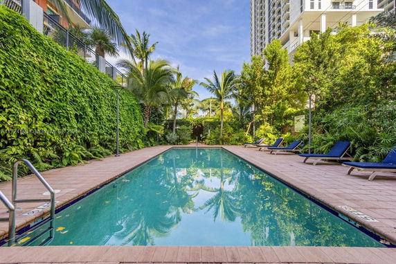 Outdoor swimming pool surrounded by lush greenery and tall buildings.