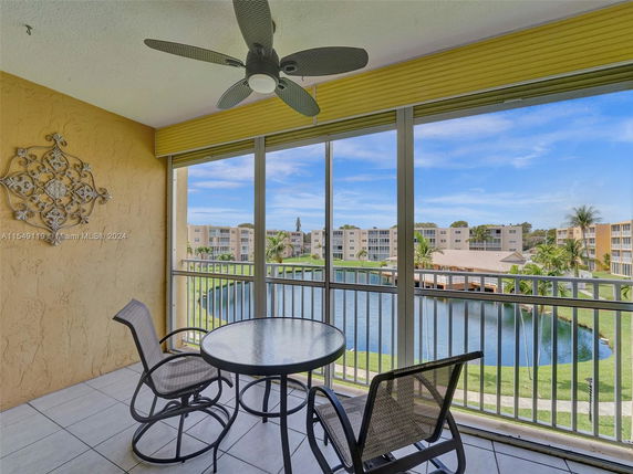 Balcony view overlooking a pond with apartment buildings and palm trees in the background.