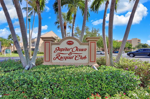 Sign for Jupiter Ocean & Racquet Club with palm trees and cars in the background.