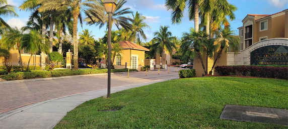 Entrance view of a condominium complex with lush palm trees and a security gate.