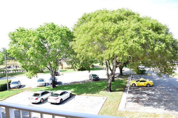 Outdoor parking area with several cars and surrounding trees.