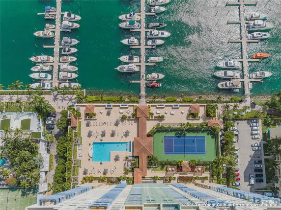 Rooftop view featuring a swimming pool, tennis court, and adjacent marina with boats.