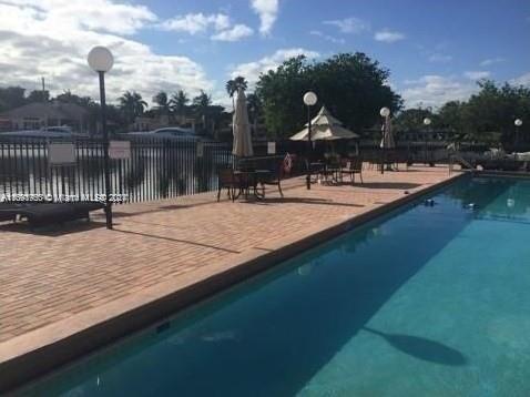Outdoor view of a pool area with surrounding trees and a waterfront in the background.