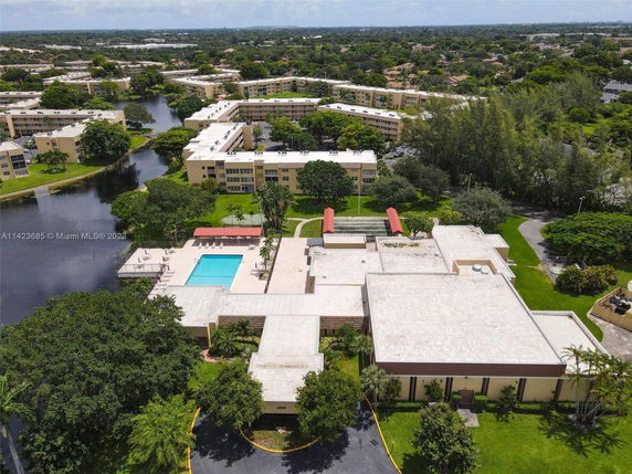 Aerial view of a multi-story residential complex with a swimming pool and green surroundings.