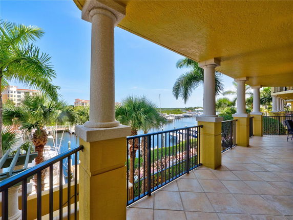 Balcony view overlooking a marina with palm trees and buildings in the background.