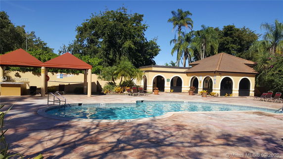 Outdoor swimming pool area with two gazebos and a building with arched openings.