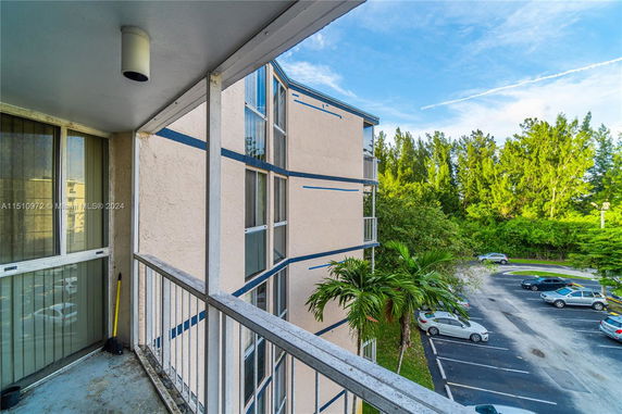 View from a building's balcony showing adjacent building and parking area with trees in the background.