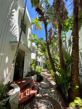 Front view of a building with a patterned walkway and surrounded by palm trees.