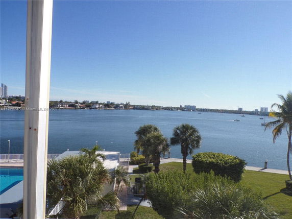 Panoramic view of water, palm trees, and distant city skyline.