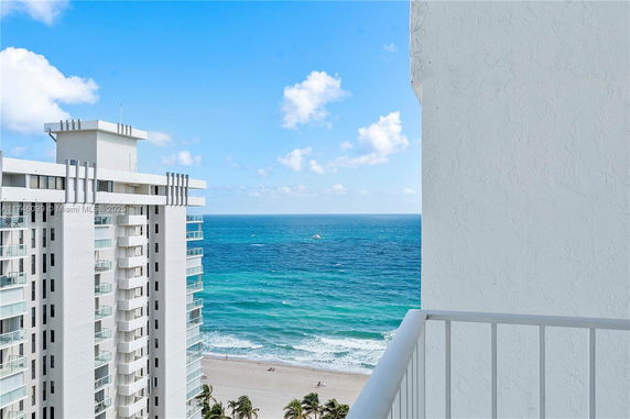 Balcony view overlooking the ocean and nearby high-rise building.