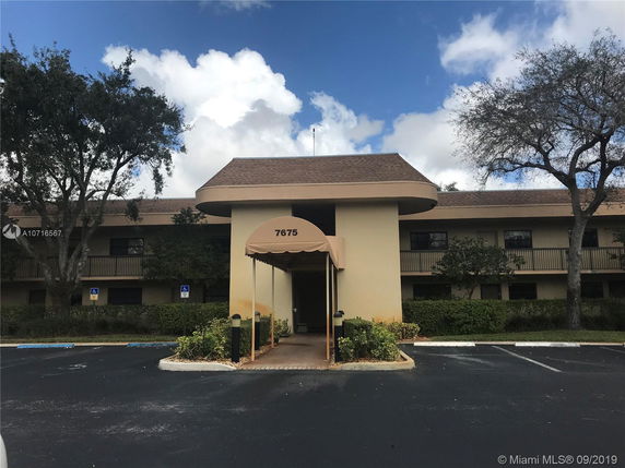 Front view of a two-story building with a covered entrance and parking area.