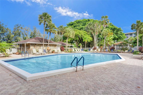Outdoor swimming pool area with lounge chairs and surrounded by trees.
