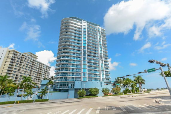 Front view of a tall, modern high-rise building with balconies and a glass facade.