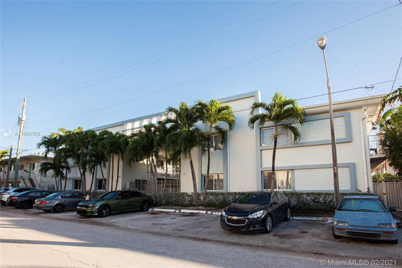 Front view of a rectangular two-story building with palm trees and parked cars in front.