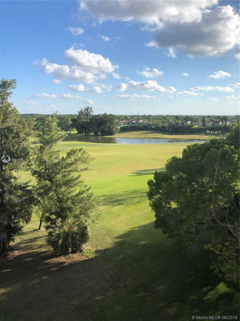 View of a grassy landscape with trees and a water feature in the distance.
