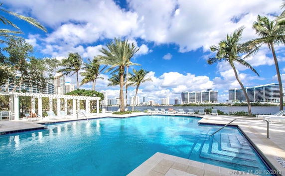 Outdoor swimming pool area with palm trees and distant view of high-rise buildings.
