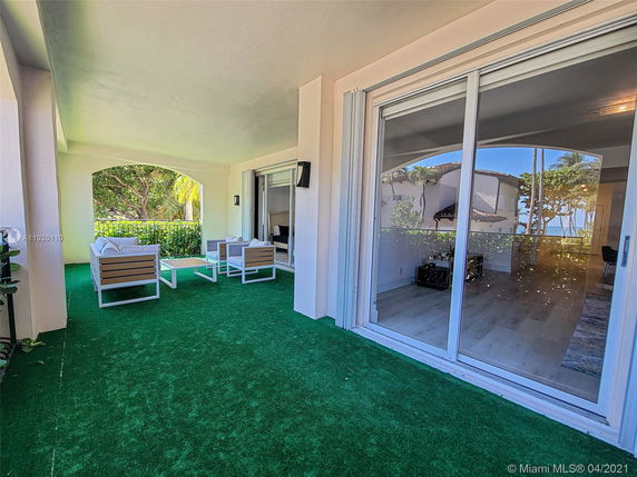 Covered outdoor patio with seating area and a view of a neighboring house and trees.