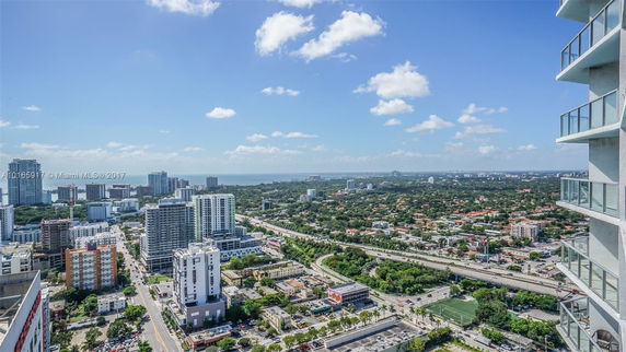 Aerial view of a cityscape featuring high-rise buildings and streets extending towards a distant coastline.