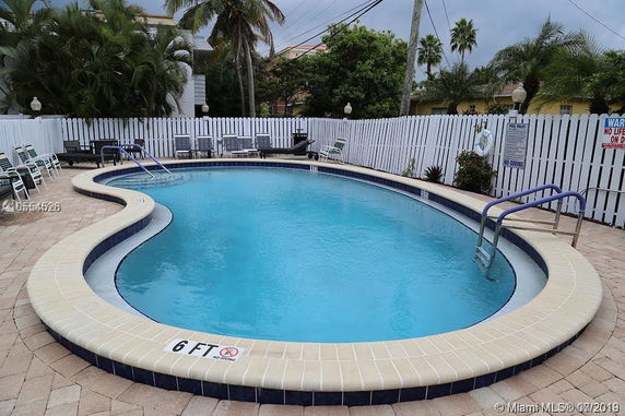 Outdoor swimming pool with surrounding fence and lounge chairs.