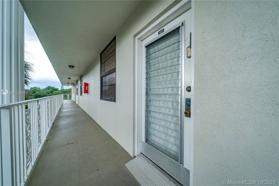 Exterior corridor of a building leading to an entrance with railing and greenery visible.