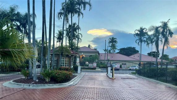 Front view of a gated community entrance with a security booth and paved driveway.