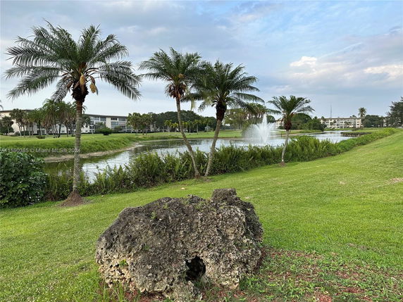 Buildings with multiple stories near a lake with palm trees and a fountain.