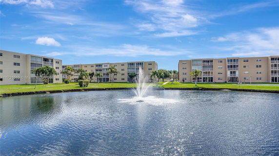 Front view of a multi-story residential building complex with a pond and fountain in the foreground.