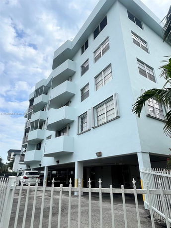 Front view of a multi-story building with balconies and a gated parking area.