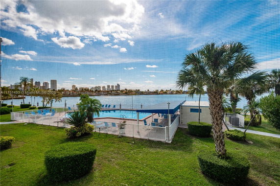 View of a swimming pool area with surrounding greenery and waterfront skyline in the background.