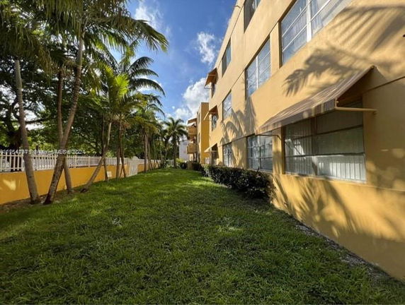 Side view of a multi-story building with windows and awnings, with a grassy area and palm trees.