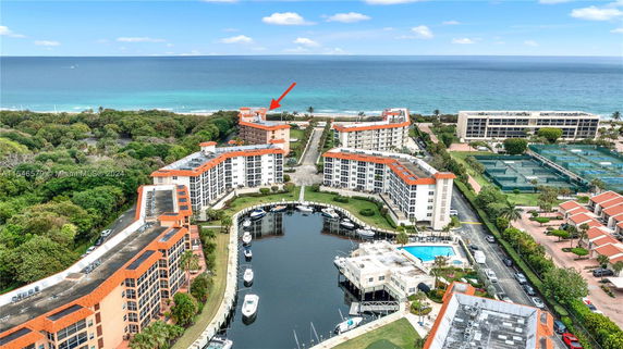 Aerial view of a waterfront residential complex with multiple buildings, a marina, and ocean in the background.