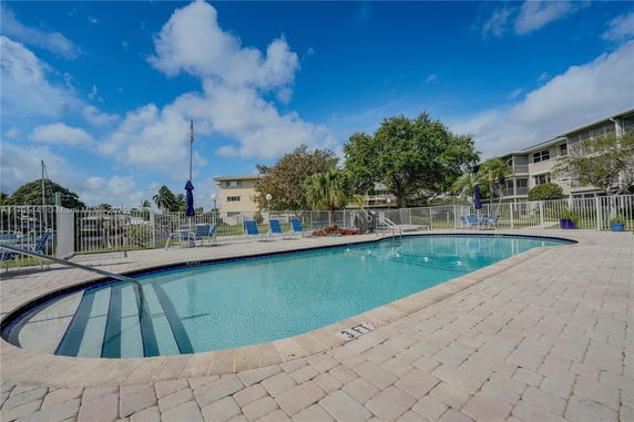 Outdoor swimming pool with a surrounding fence and lounge chairs.