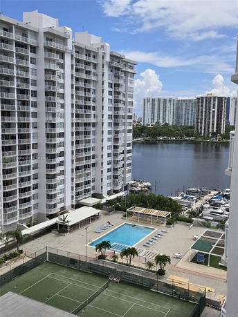 View of an apartment complex with a swimming pool and tennis court, overlooking a waterway with boats.