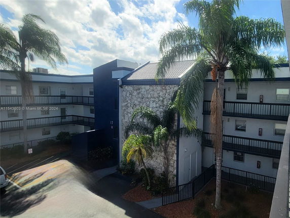 View of a multi-story building with palm trees and a parking area in the foreground.
