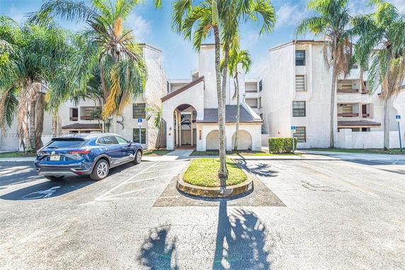 Front view of a multi-story apartment building with arched entrance and parking area.