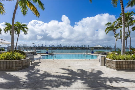 Outdoor swimming pool area with a view of the waterfront and a city skyline in the background.