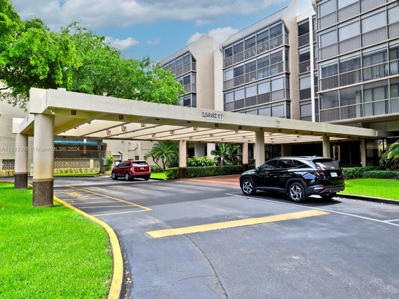 Covered outdoor parking area in front of a multi-story building.