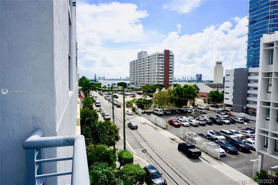 View from a building overlooking a street with parked cars and high-rise apartments in the background.