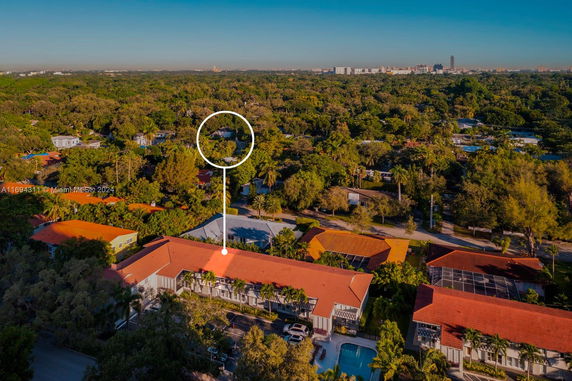 Aerial view showing buildings with red roofs surrounded by lush green vegetation and distant city skyline.