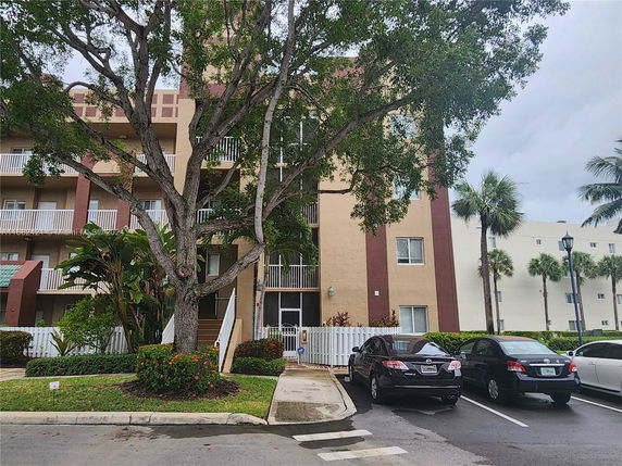 Front view of a multi-story residential building with balconies and adjacent parking area.