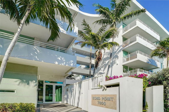 Front view of a modern multi-story building with balconies and palm trees.