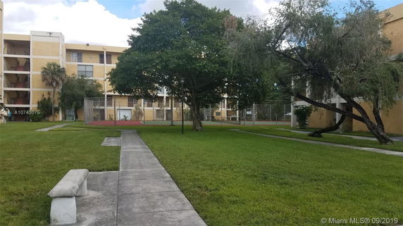 View of a multi-story building with a beige exterior, surrounded by grass and trees.