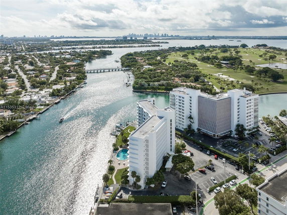 Aerial view of a waterway surrounded by residential buildings, a golf course, and distant city skyline.