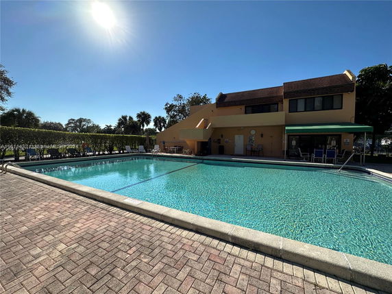Outdoor swimming pool with surrounding patio and a multi-story building nearby.