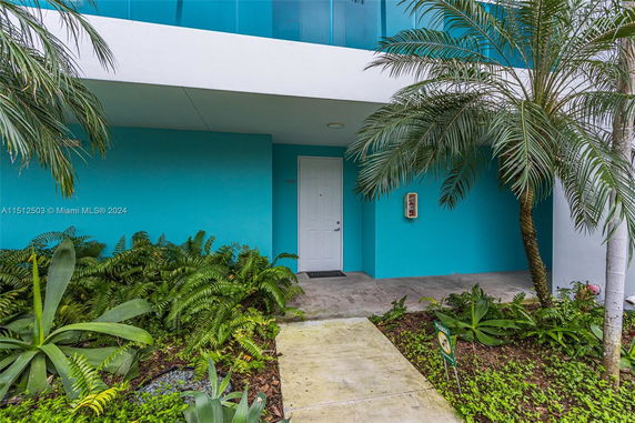 Front view of a building entrance with a teal exterior and surrounding foliage.