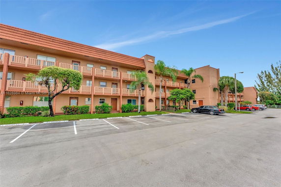 Front view of a multi-story apartment building with balconies and a parking area.