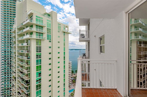 View from a balcony of an apartment building overlooking another tall building and water in the distance.