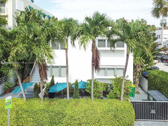 Front view of a small multi-story building with palm trees and umbrellas.