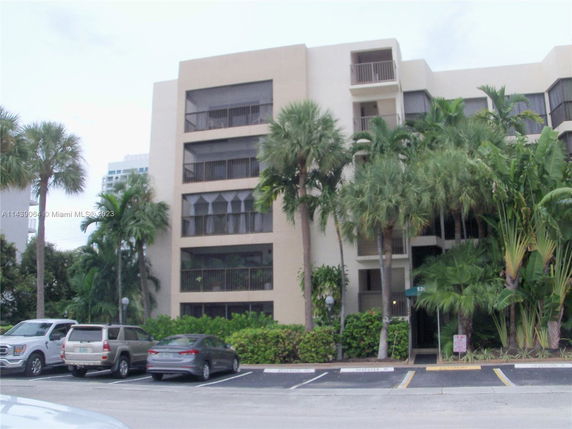 Front view of a multi-story residential building with balconies and parking spaces in front.